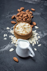 Almond slices and whole nut in wooden bowls with milk jug for healthy nutrition