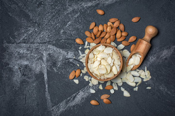 Top view of almond slices and whole nut in wooden bowl as ingredient for confectionery on black...