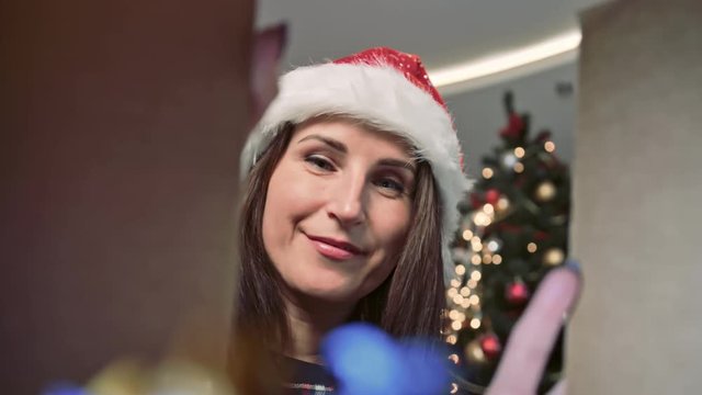 Beautiful European woman wearing Santa Claus hat opening gift box and smiling looking inside