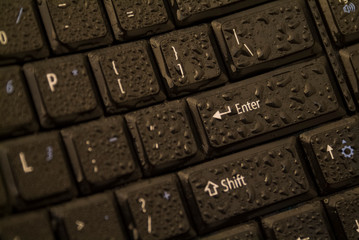 black keyboard with a wet surface focused and zoomed on the enter key