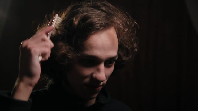 funny man combing his long curly hair with hairbrush in the dark room