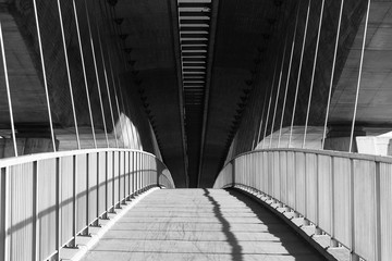 Rising path on the pedestrian bridge under the highway bridge in black and white with long shadows