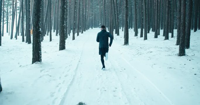 WIDE TRACKING Adult fit Caucasian male jogging on winter forest trail. 4K UHD 60 FPS SLO MO