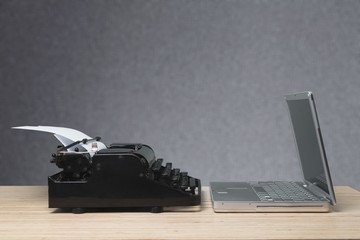 Old typewriter and laptop on wooden table