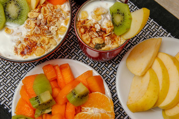 Healthy food, various seeds, integral cereals and dried fruits in yogurt. Fresh fruit, apple, orange, kiwi and persimmon. Wooden table with modern black and white mat and candle light.