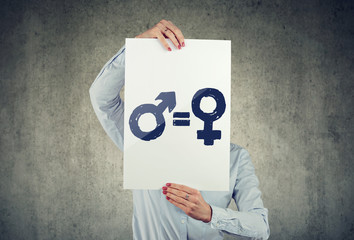 Business woman holding a white paper with male and female symbol on gray wall background.