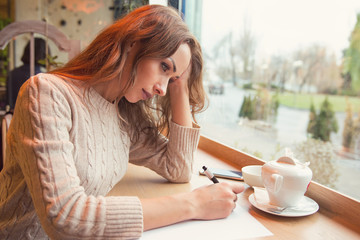 Sad young woman writing letter with broken heart