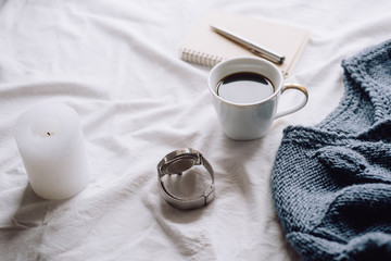 Cup coffee , blue knitted sweater, notebook with pen,  clock, candle on bed, top view. Women clothing. Flat lay, cozy concept