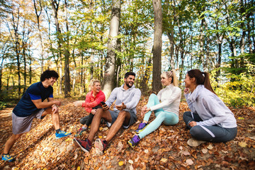 Happy small group of friends sitting on the ground in the woods and resting from the running. Autumn time.