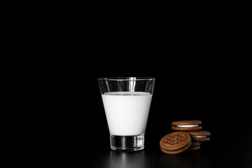 Glass of milk and chocolate cookies on black background