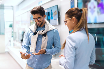 Fototapeta premium Smiling cute multicultural couple standing in tech store and at price for new television they want to buy.