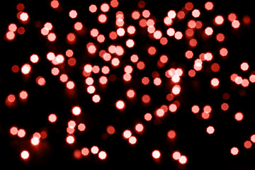 Fototapeta na wymiar Abstract living coral bokeh texture on black background. Defocused sparkles. Color of the year.