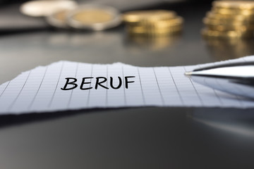 Beruf auf einem Zettel mit Stift vor Geldmünzen