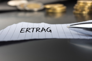 Ertrag auf einem Zettel mit Stift vor Geldmünzen