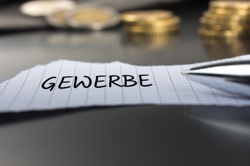 Gewerbe auf einem Zettel mit Stift vor Geldmünzen