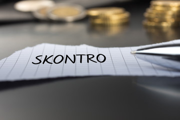Skontro auf einem Zettel mit Stift vor Geldmünzen
