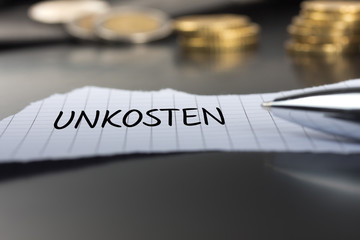 Unkosten auf einem Zettel mit Stift vor Geldmünzen