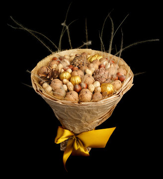 An original gift in the form of a bouquet consisting of various nuts and cones, wrapped with kraft paper and tied with a yellow satin ribbon on black background