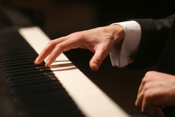 Fototapeta premium Hands on piano. The pianist plays the piano. Piano keys on black background