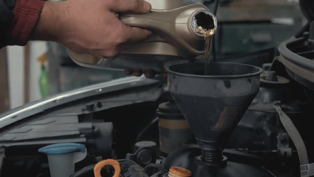 Car maintenance servicing mechanic pouring new oil lubricant into the car engine. Pouring fresh new clean synthetic oil into car engine. Change engine oil of your car.