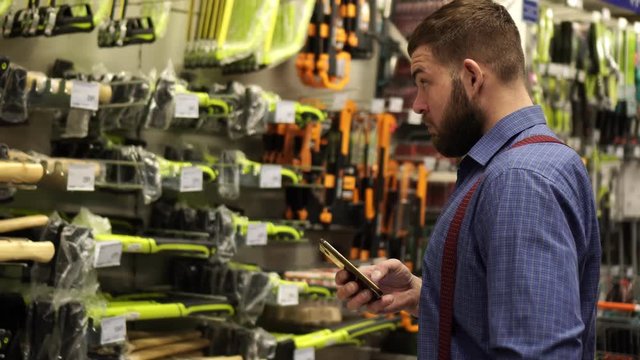 A Man In A Hardware Store Uses A Smartphone.