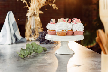 Fresh delicious cupcakes with white cream and colored macarons on a white tray on marble table.
