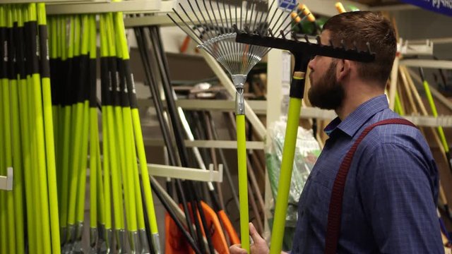 A man in a hardware store. The buyer chooses a farmer garden tool.