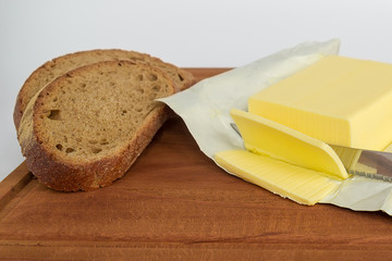A few slices of yellow butter cut off from a large piece with a knife on a brown wooden cutting...