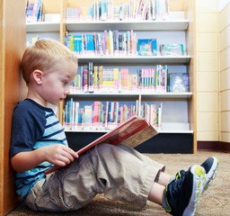 Preschool child reading a book at the library