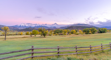 A distant snow capped mountain range in front of rolling green farm land