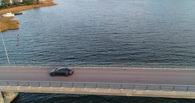 Car on a bridge, C4K aerial, tilt down, drone shot, following a car driving on a asphalt road, in the archipelago, on a cloudy, autumn day, in Varsinais-suomi, Finland