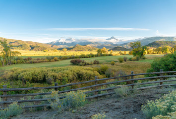 The sun is about to set over a ranch in the colorado mountains filled with cows and surrounded by fences