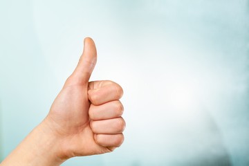 Closeup of male hand showing thumbs up sign against  background
