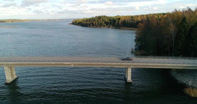 Car on a bridge, C4K aerial, tracking, drone shot, following a car driving on a asphalt road, in the archipelago, on a cloudy, day, in Varsinais-suomi, Finland