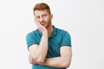 Waist-up shot of bored and tired gloomy redhead guy with bristle in green polo-shirt, leaning face...