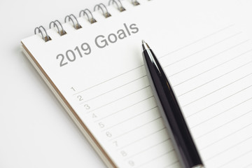New year 2019 resolution or writing goals, to do list or work target plan concept, black pen on notepad with header as 2019 Goals with list of numbers on white office desk
