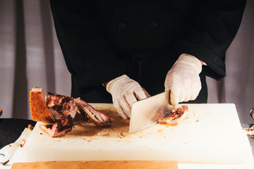 Hands of a male chops roast pork with a cleaver at a holiday party