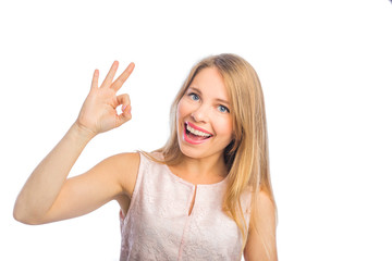 Fototapeta premium Young beautiful blond woman in a sleeveless blouse shows okay with one hand and smiles, shooting close-up on an isolated background.