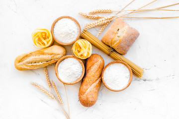 Fototapeta na wymiar Homemade fresh bread and pasta near flour in bowl and wheat ears on white stone background top view