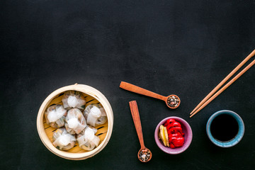 Chinese steamed dumplings Dim Sum with sweet paper and spices in bamboo steamer on black background top view mock up