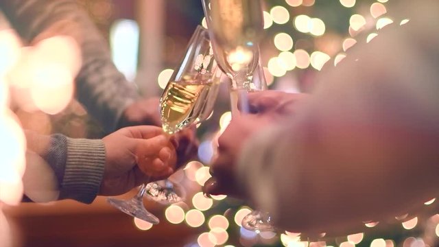 Toasting champagne. Group of people celebrating Christmas party with champagne. Glasses with sparkling wine over glowing background. Slow Motion 4K UHD video footage. 3840X2160