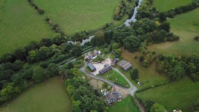 Aerial farm house and barns along river Wales. Beautiful green, rock fences, hedgerow and forest tree meadows and rural farms. Rolling hills and gentle valley. Nature and history mingle in harmony.