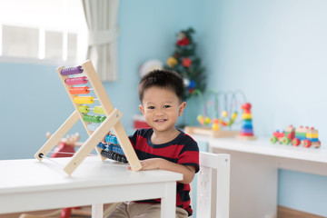 Asian Toddler baby boy learns to count. Cute child playing with abacus toy. Little boy having fun indoors at home. Educational concept for Toddler baby.