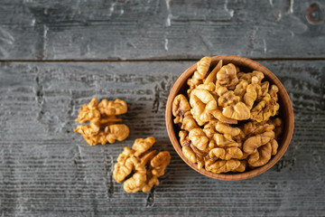 Walnut kernels and a clay bowl with peeled walnuts on a rustic table. The view from the top.