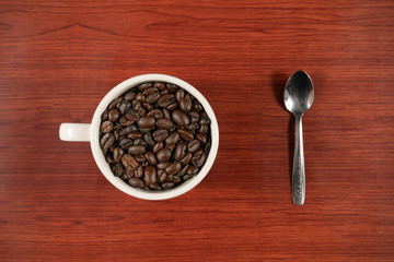 Coffee beans in white cup and spoon with wooden background