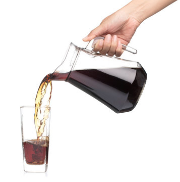 Hand pouring cola from glass jug to glass isolated on a white background