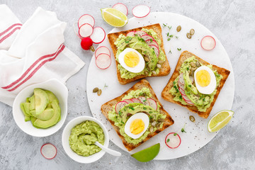 Toasts with avocado guacamole, fresh radish, boiled egg, chia and pumpkin seeds. Diet breakfast. Delicious and healthy plant-based food. Flat lay. Top view
