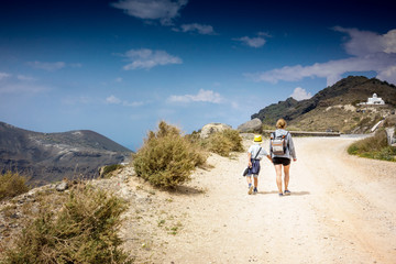 Mother with son walking on dirt road leading to mountain; Santorini island; Greece