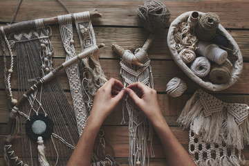 Female hands weaving macrame on a wooden table. Do it yourself. Top view. - obrazy, fototapety, plakaty