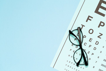 Eye test, eye examination. Glasses with transparent optical lenses on eye test chart on blue...